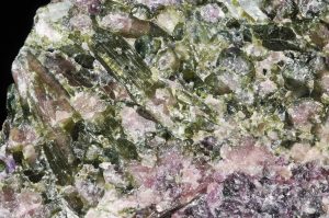 Closeup view of rock with elongated glassy green crystals intergrown with light purple glassy grains.